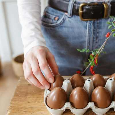 Photo by Polina Tankilevitch A person arranging chocolate eggs in a carton on a wooden table, indoors.