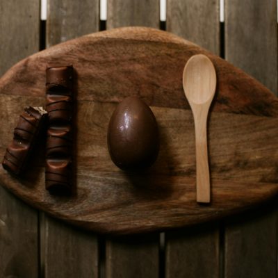 Photo by ROMAN ODINTSOV Flat lay composition of chocolate egg and wooden spoon on a rustic tray.